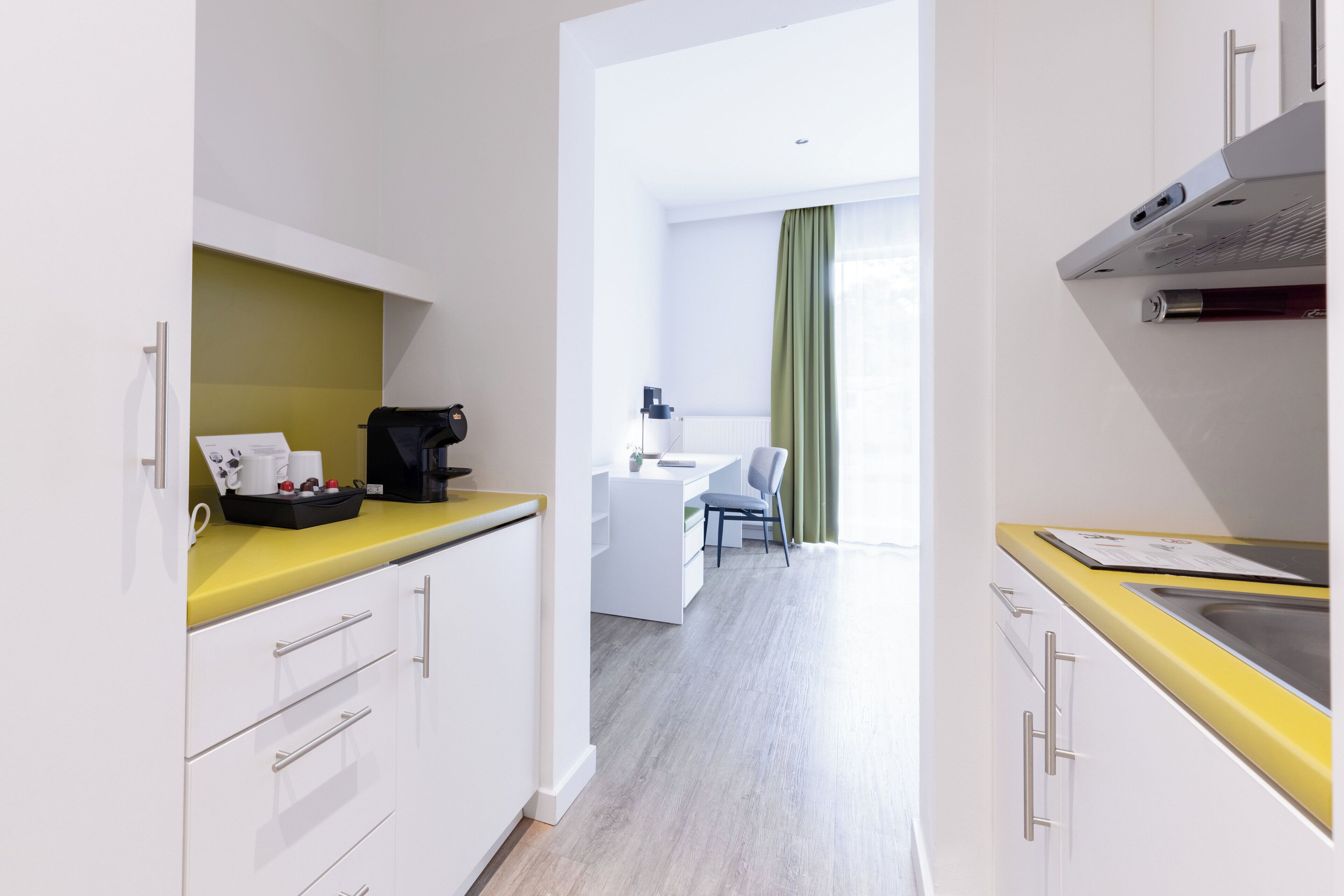 A modern kitchen with white cabinets, a yellow countertop, and a view into a dining area with a green curtain.