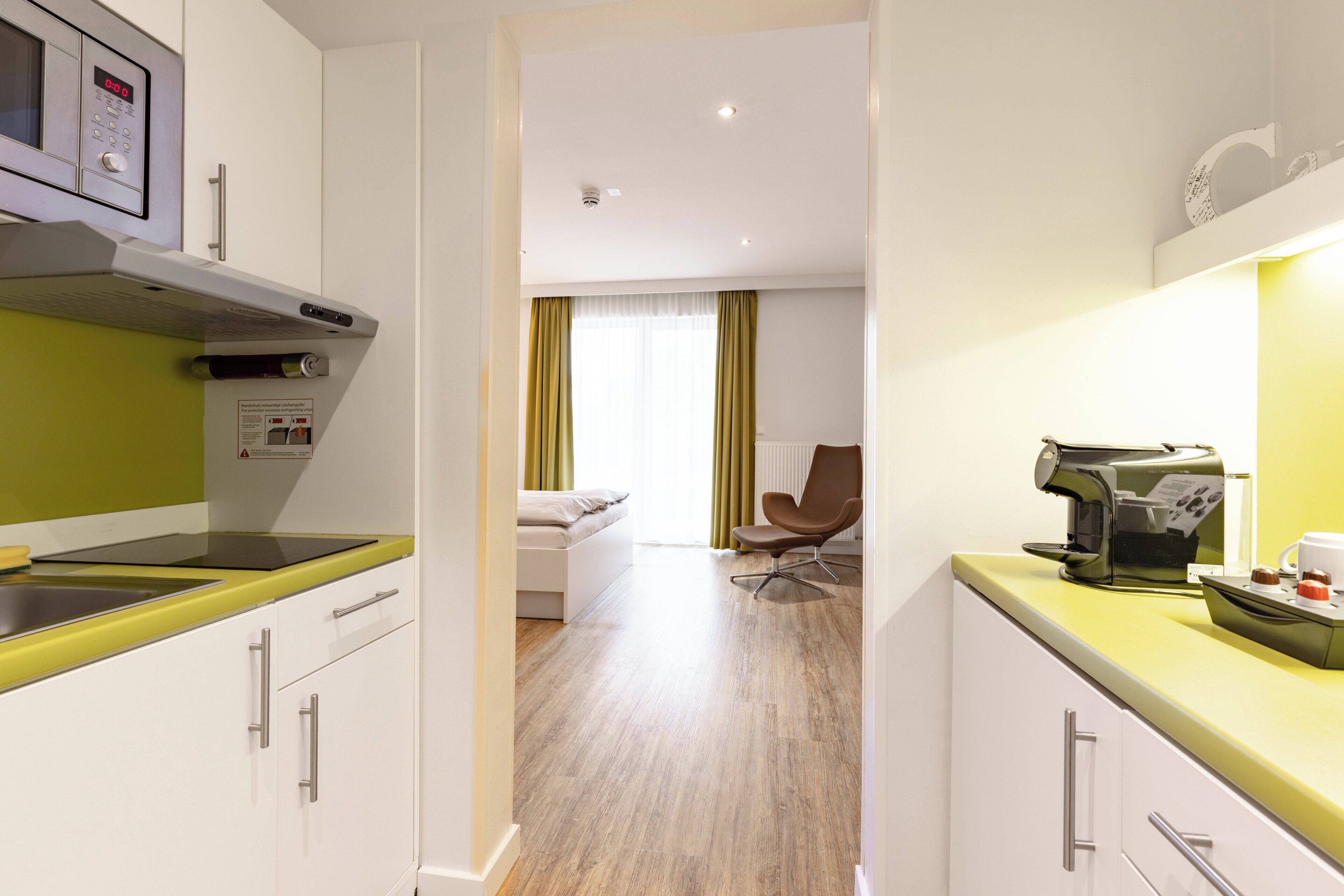 A modern kitchen with a microwave, coffee machine, and a dining area with a chair and a bed.