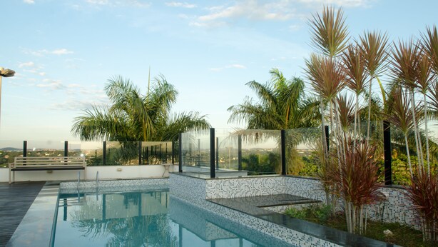 Una piscina infinita en la azotea con vistas despejadas del horizonte urbano, rodeada de palmeras y arquitectura moderna.