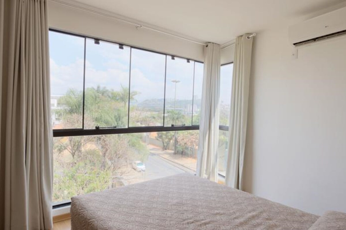A bedroom with a large window, a bed, and a view of a road and trees.