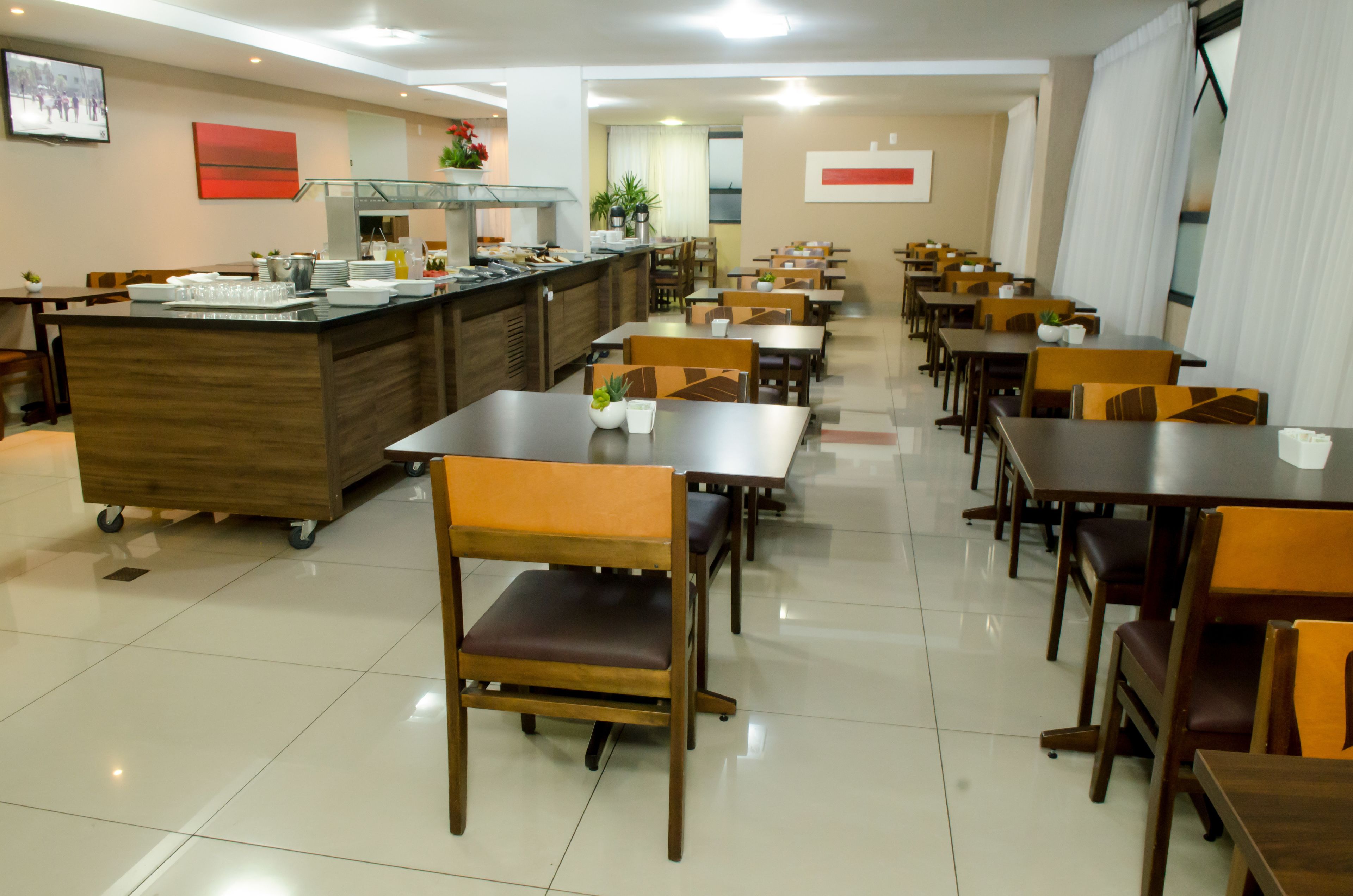 Un grand espace dédié à la salle à manger, avec de nombreuses tables et chaises, un buffet central et un sol carrelé, propre et bien entretenu.