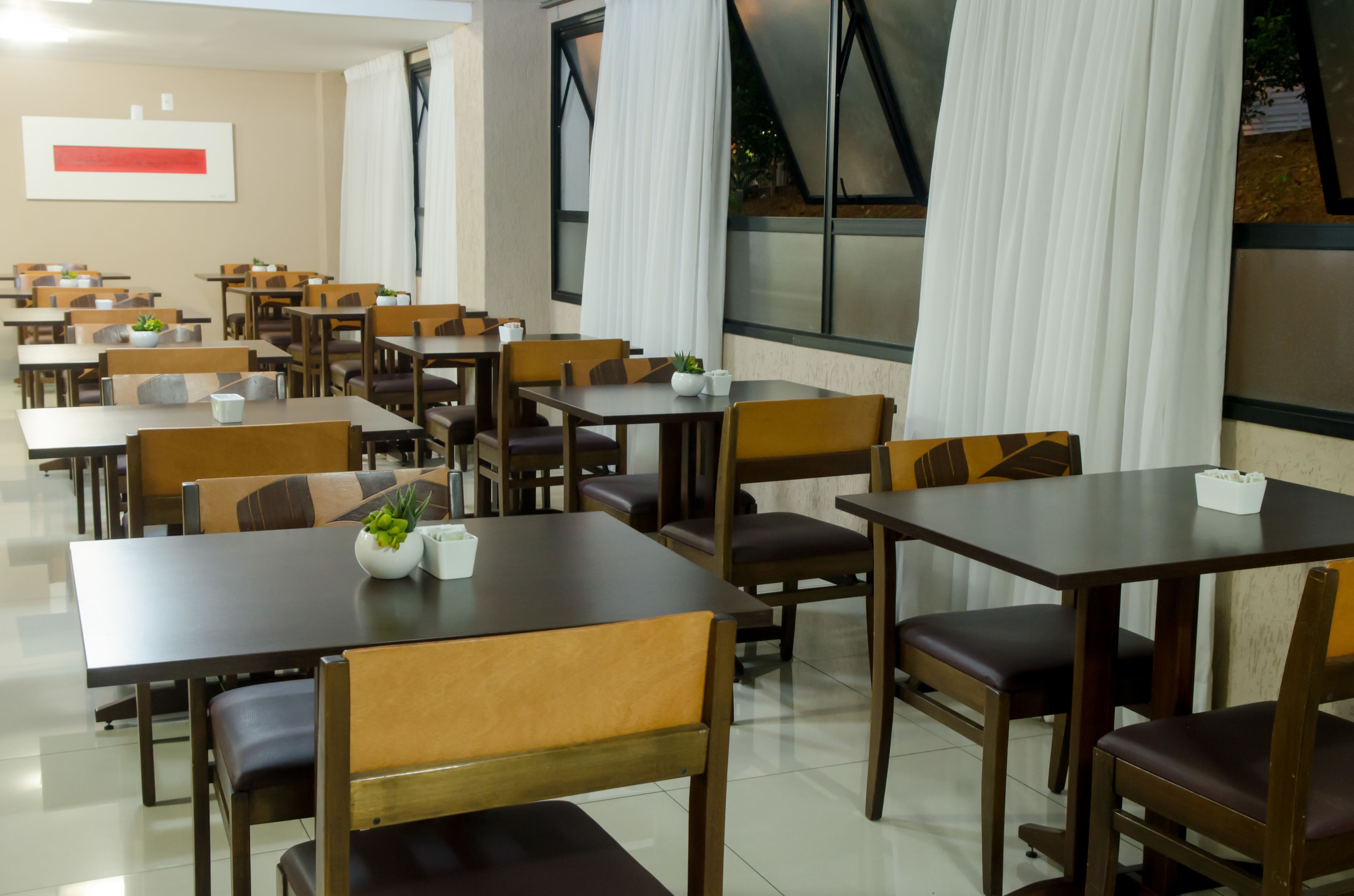 A spacious dining area with multiple tables and chairs, large windows with curtains, and a modern interior design.