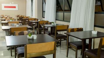 A spacious dining area with multiple tables and chairs, large windows with curtains, and a modern interior design.