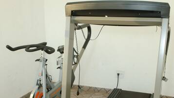 Uma bicicleta ergométrica e uma esteira em um espaço com piso ladrilhado e paredes brancas.