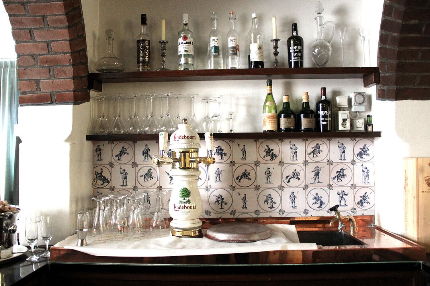 A bar area with a beer tap, shelves of liquor bottles, and a tiled wall with historical figures.