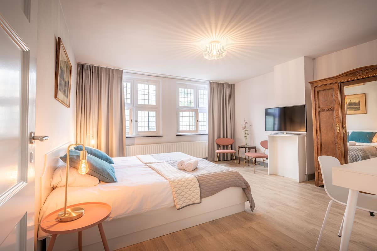 A modern hotel room with a large bed, a desk, a television, and a wardrobe.