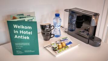 Habitación de hotel con un cartel de bienvenida, una taza de café, una botella de agua, una tetera y una bandeja con condimentos.