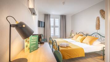 Une chambre d’hôtel avec un lit, un bureau avec une lampe, une chaise, une télévision et une fenêtre avec des rideaux.