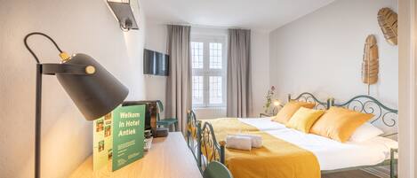 A hotel room with a bed, a desk with a lamp, a chair, a television, and a window with curtains.