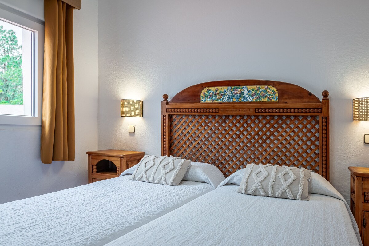 A double bed with a wooden headboard, two bedside tables, and a window with curtains.