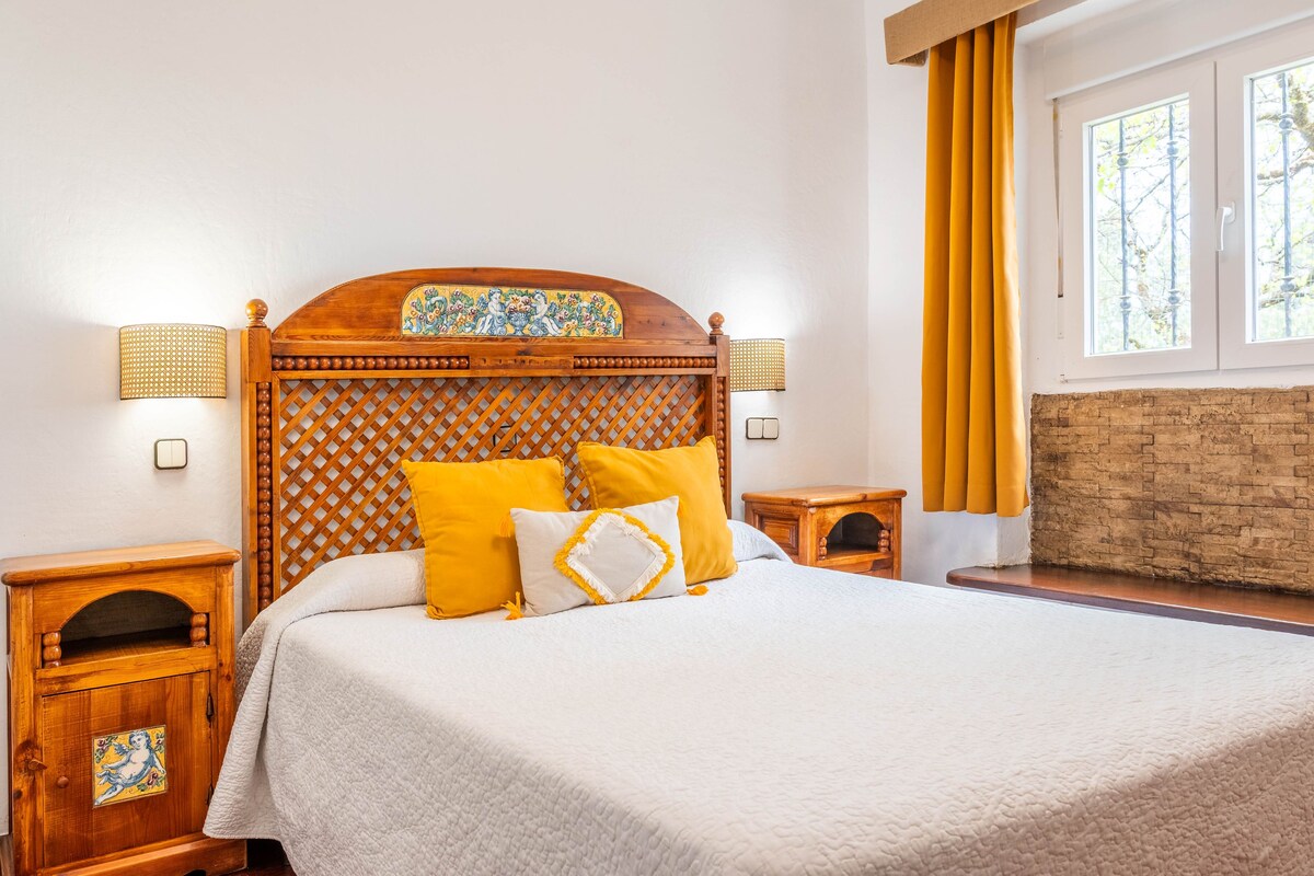 A neatly made bed with a wooden headboard, two bedside tables, and a window with curtains.