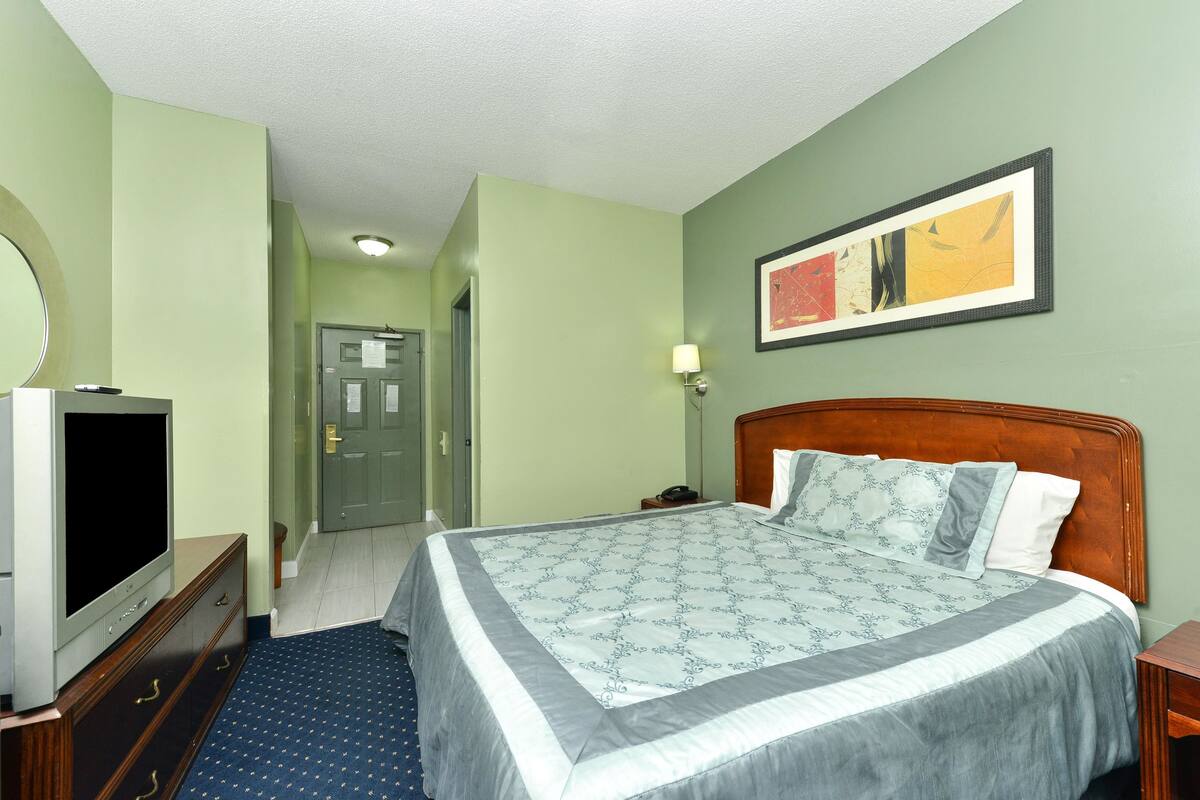 Ein Hotelzimmer mit einem großen Bett, einem Fernseher auf einem Schminktisch und einem Gemälde an der Wand.
