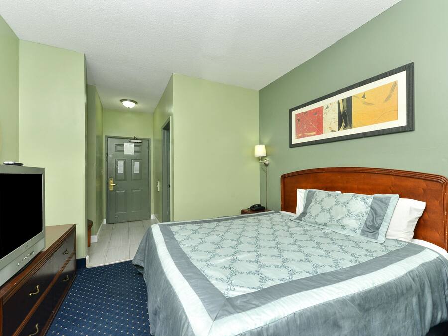 Une chambre d’hôtel avec un grand lit, un téléviseur posé sur une commode et un tableau accroché au mur.