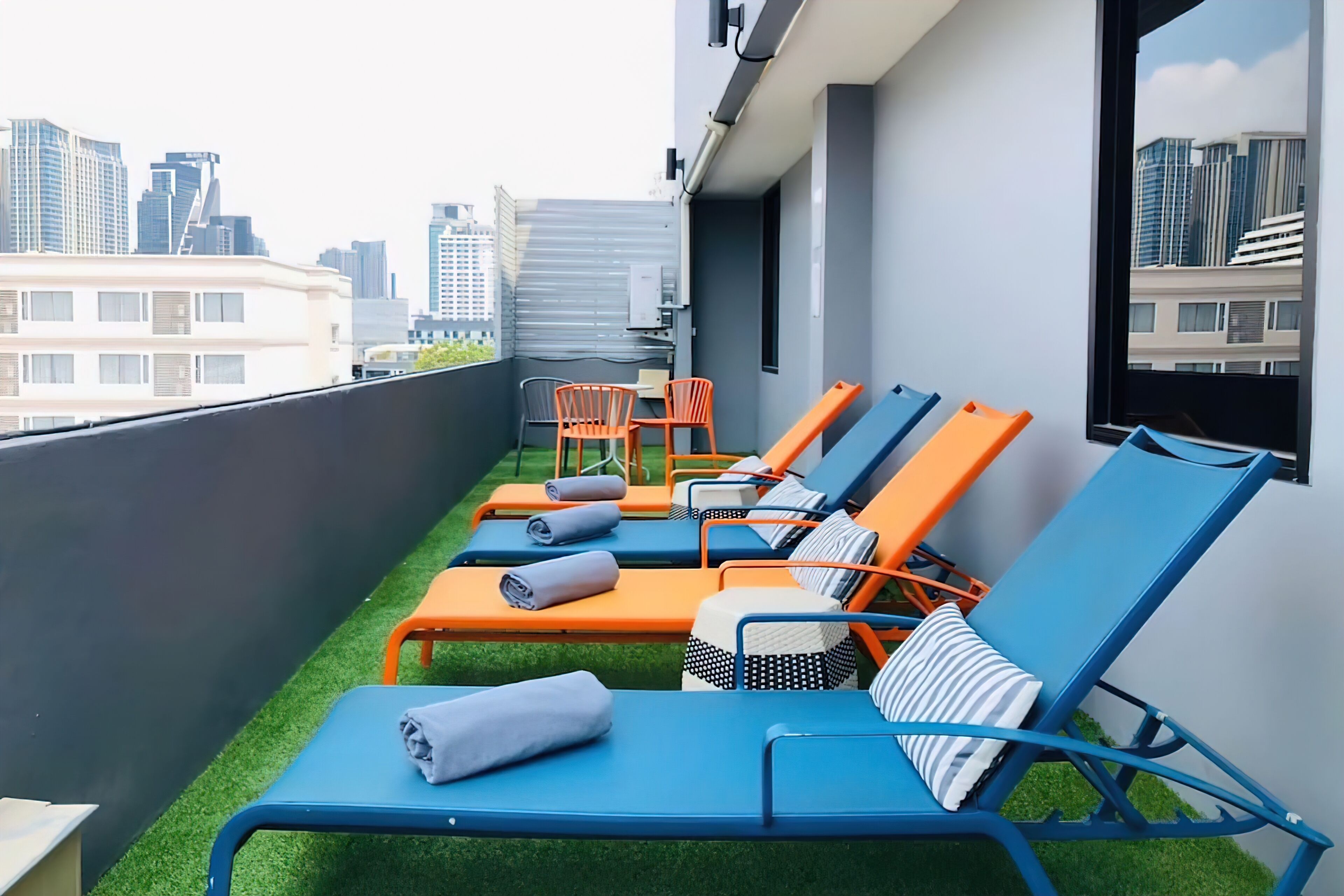 Un salon sur le toit, avec des fauteuils bleus et orange, une petite table et une vue sur le panorama de la ville.