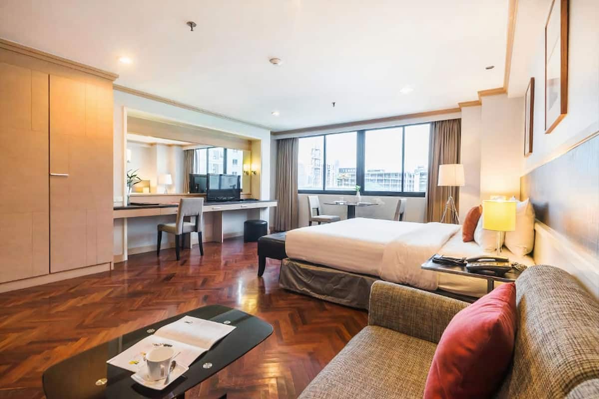 A hotel room with a large bed, a desk with a chair, a sofa, and a small table with a cup and saucer.