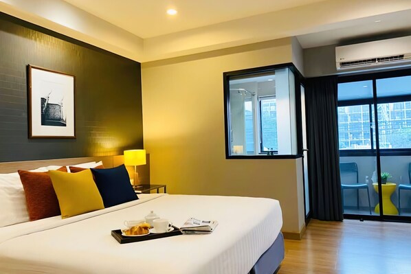 Ein Hotelzimmer mit einem großen Bett, einem Nachttisch mit Lampe, einem gerahmten Bild an der Wand und einem Balkon mit Sitzgelegenheiten.