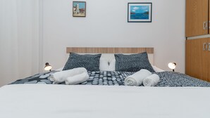 A neatly made bed with rolled towels, a patterned bedspread, and two wall-mounted lamps. - Apartments Vojin (Okrug)