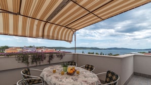 A terrace with a table set for two, a view of the sea, and a building in the background. - Apartments Vojin (Okrug)