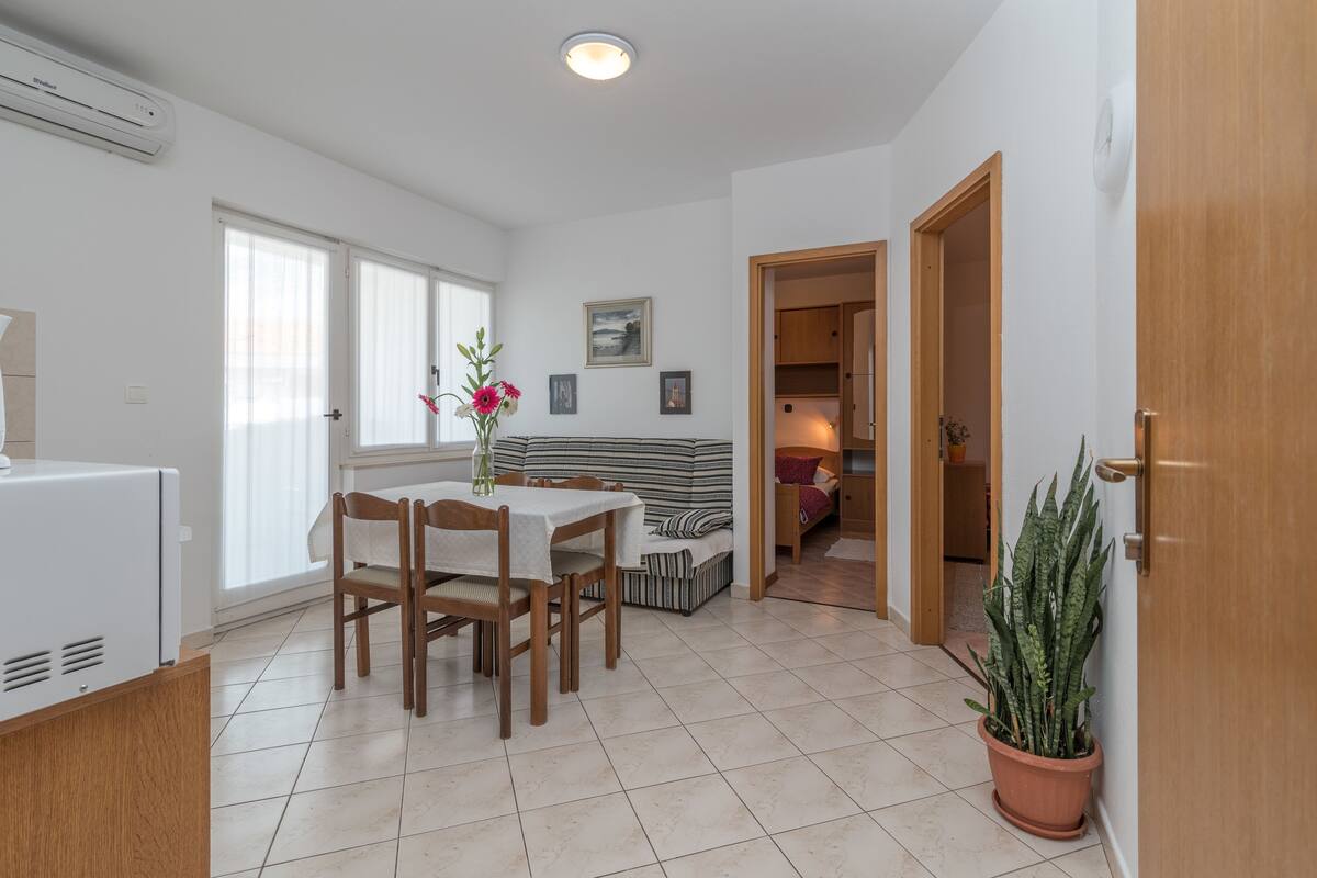A modern kitchen with a built-in refrigerator, a dining area with a table and chairs, and a living area with a sofa and a potted plant.