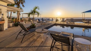 A rooftop pool area with lounge chairs, a small table, and a view of the ocean at sunset. - MariaMar Suites (San José del Cabo)