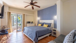 A bedroom with a bed, a ceiling fan, a TV, a desk, and a window with curtains. - MariaMar Suites (San José del Cabo)