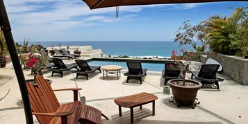 Un patio exterior con sillones de descanso, piscina y vista al océano.