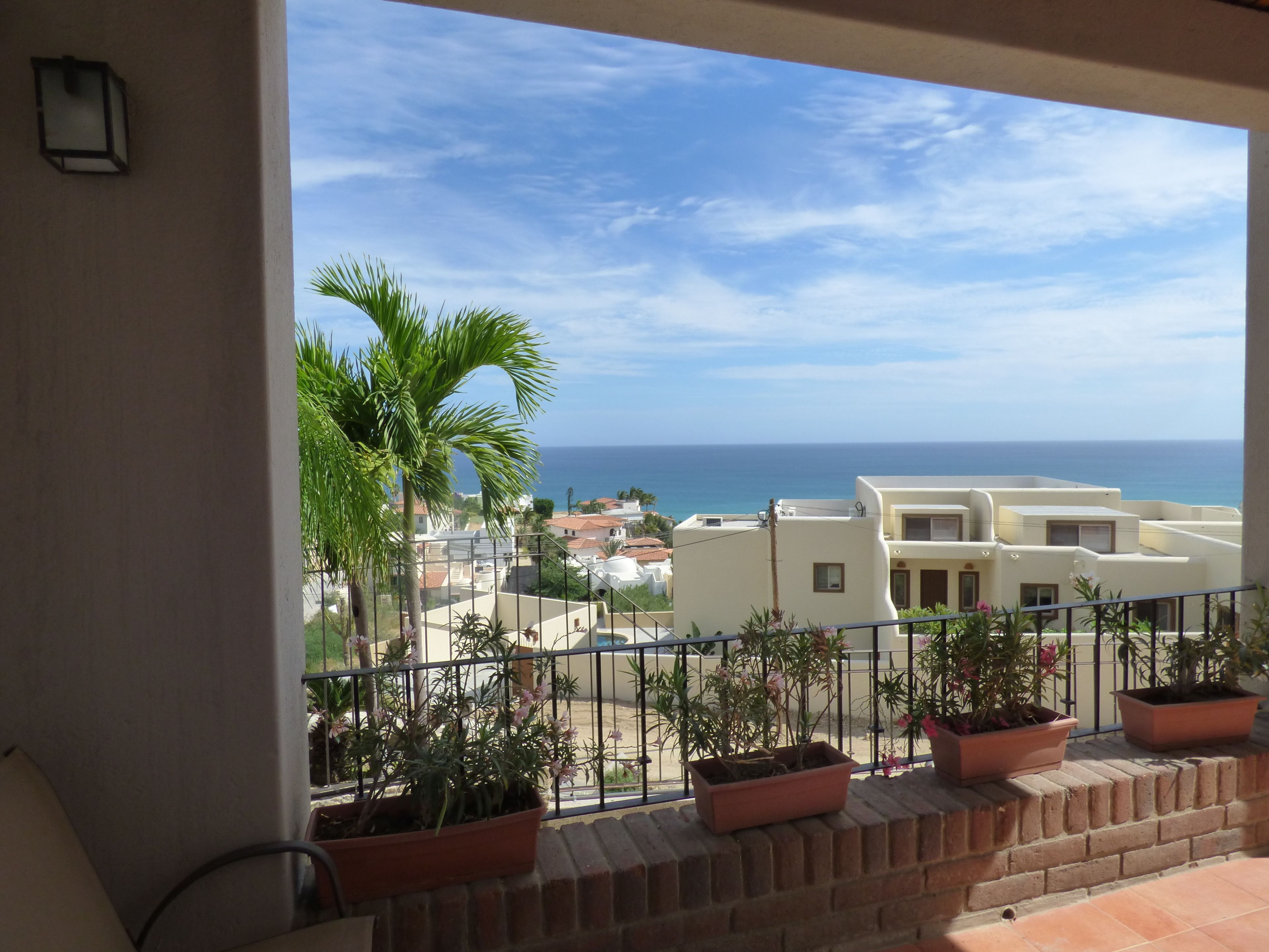 Ein Balkon mit Blumentöpfen, Blick auf das Meer und Gebäude im Hintergrund.