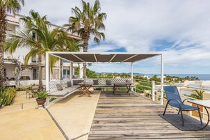 Una terraza de madera con mobiliario exterior, un espacio de estar cubierto y vista al océano.