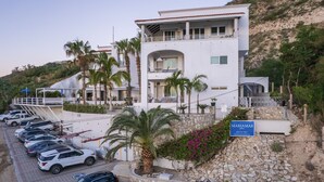 A modern two-story building with a stone facade, a balcony, and a parking area with several cars. - MariaMar Suites (San José del Cabo)