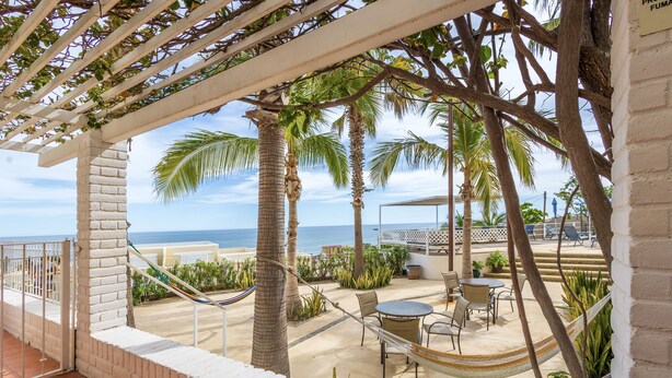 A patio with a hammock, outdoor seating, palm trees, and a view of the ocean. - MariaMar Suites (San José del Cabo)