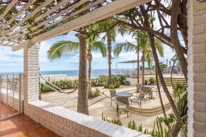 Un patio con hamaca, mobiliario exterior, palmeras y vista al océano.