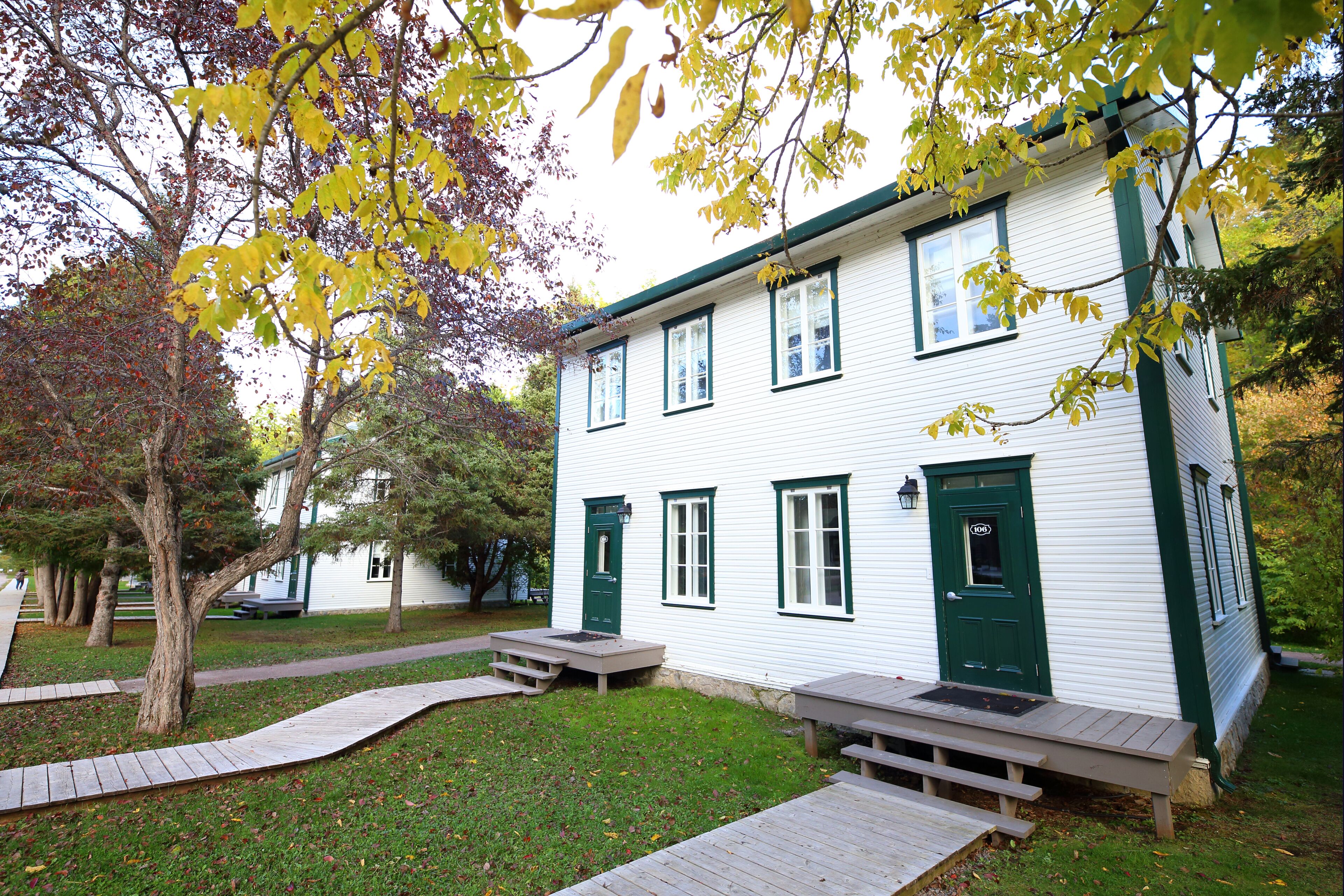 A white building with green trim, a front door, and a small porch area with benches.