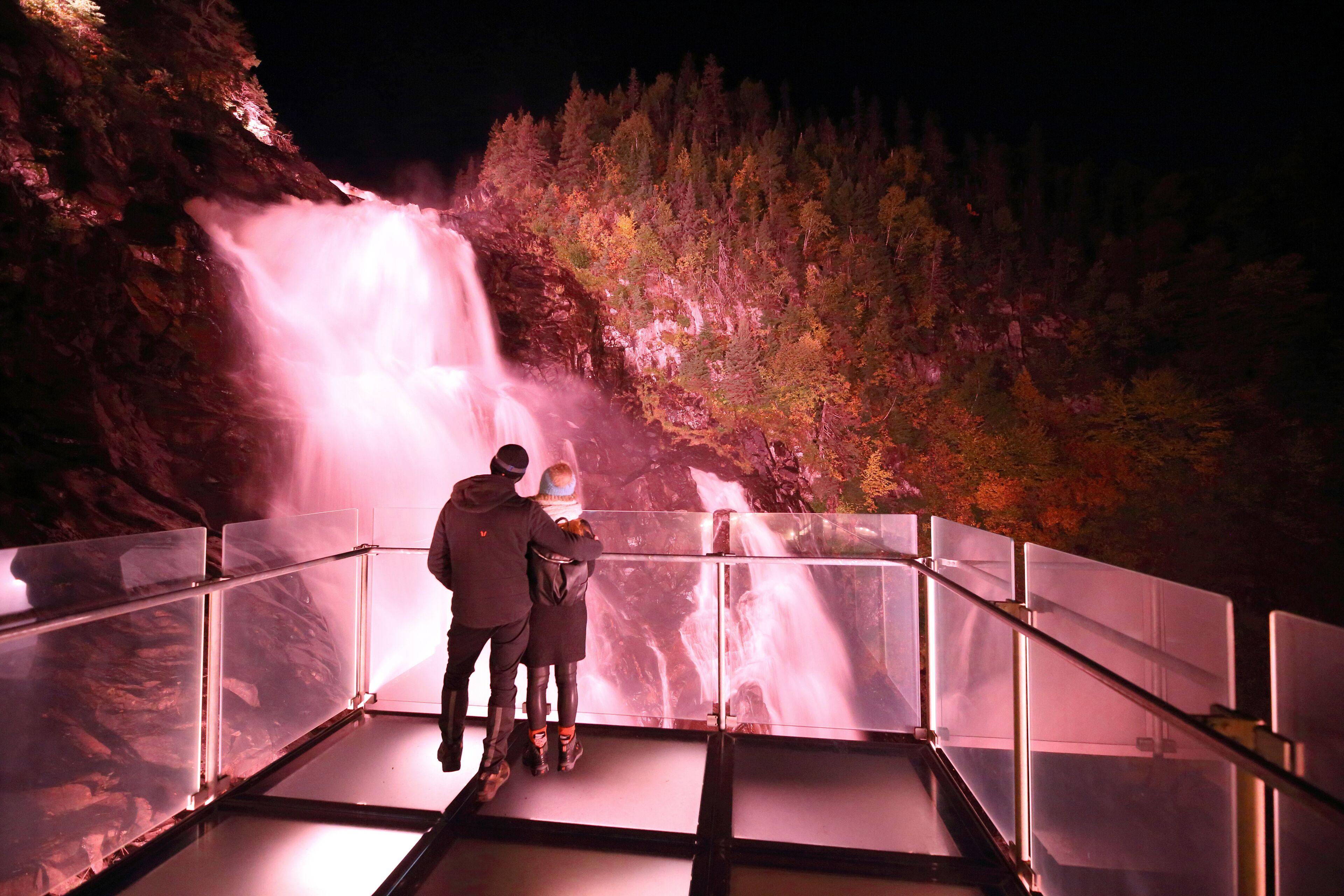 A couple standing on a glass railing overlooking a waterfall.