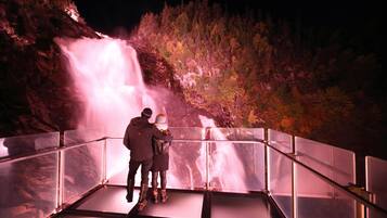 A couple standing on a glass railing overlooking a waterfall.