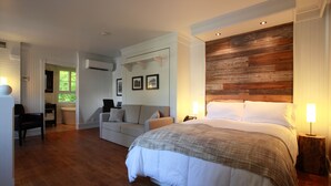Une chambre avec un grand lit, un mur d’accent en bois, un canapé blanc recouvert de tissu et un bureau avec une chaise.