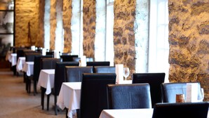 Une rangée de tables et de chaises dans un restaurant aux murs de pierre et aux grandes fenêtres.