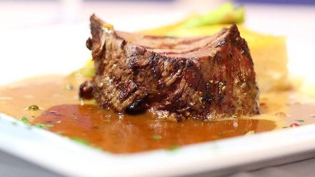 Een steak met saus op een bord, met een glas rode wijn op de achtergrond.