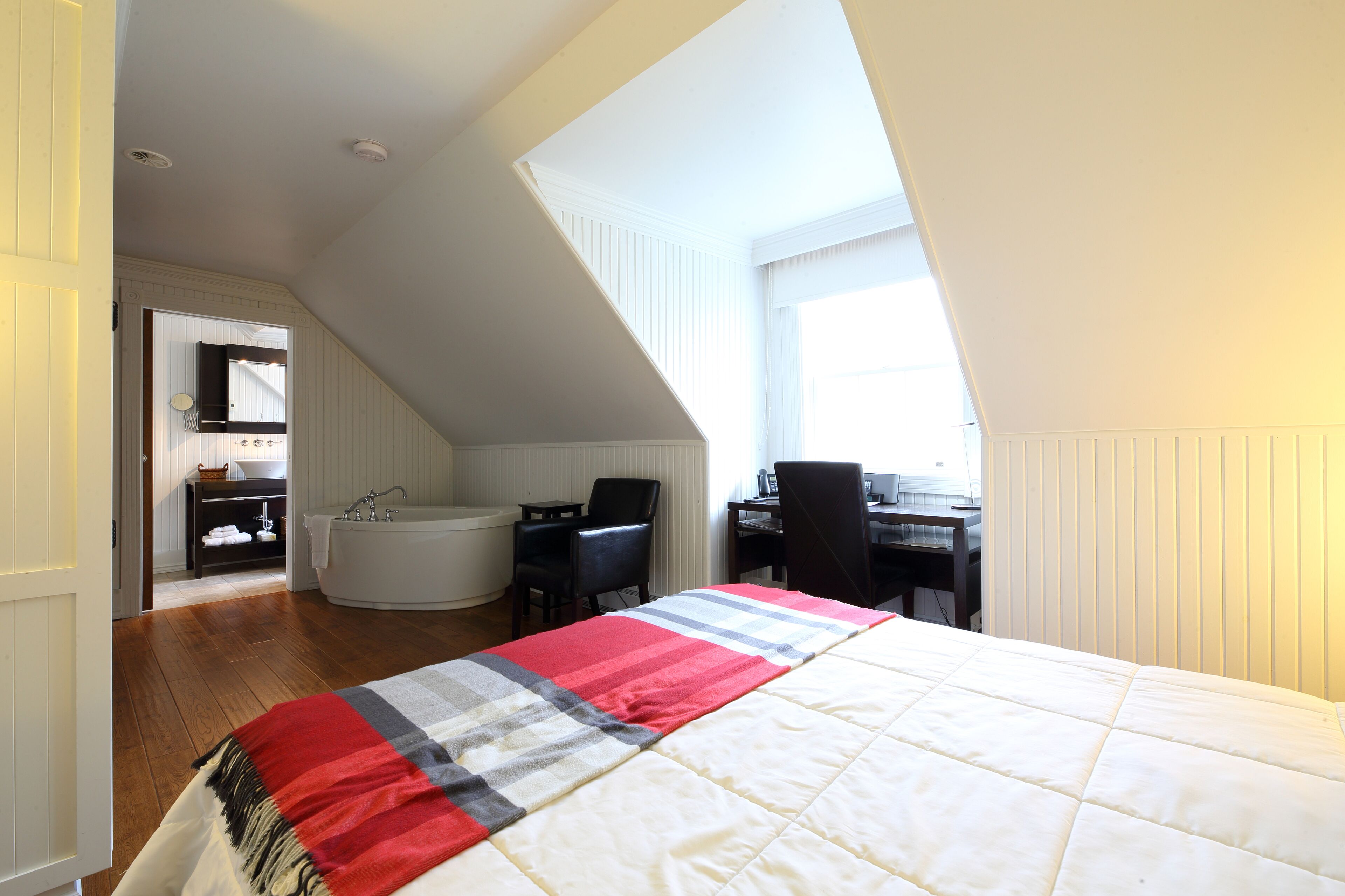 Une chambre à coucher avec un grand lit, un bureau, une chaise, une baignoire et une salle de bain équipée d’un lavabo et d’un miroir.