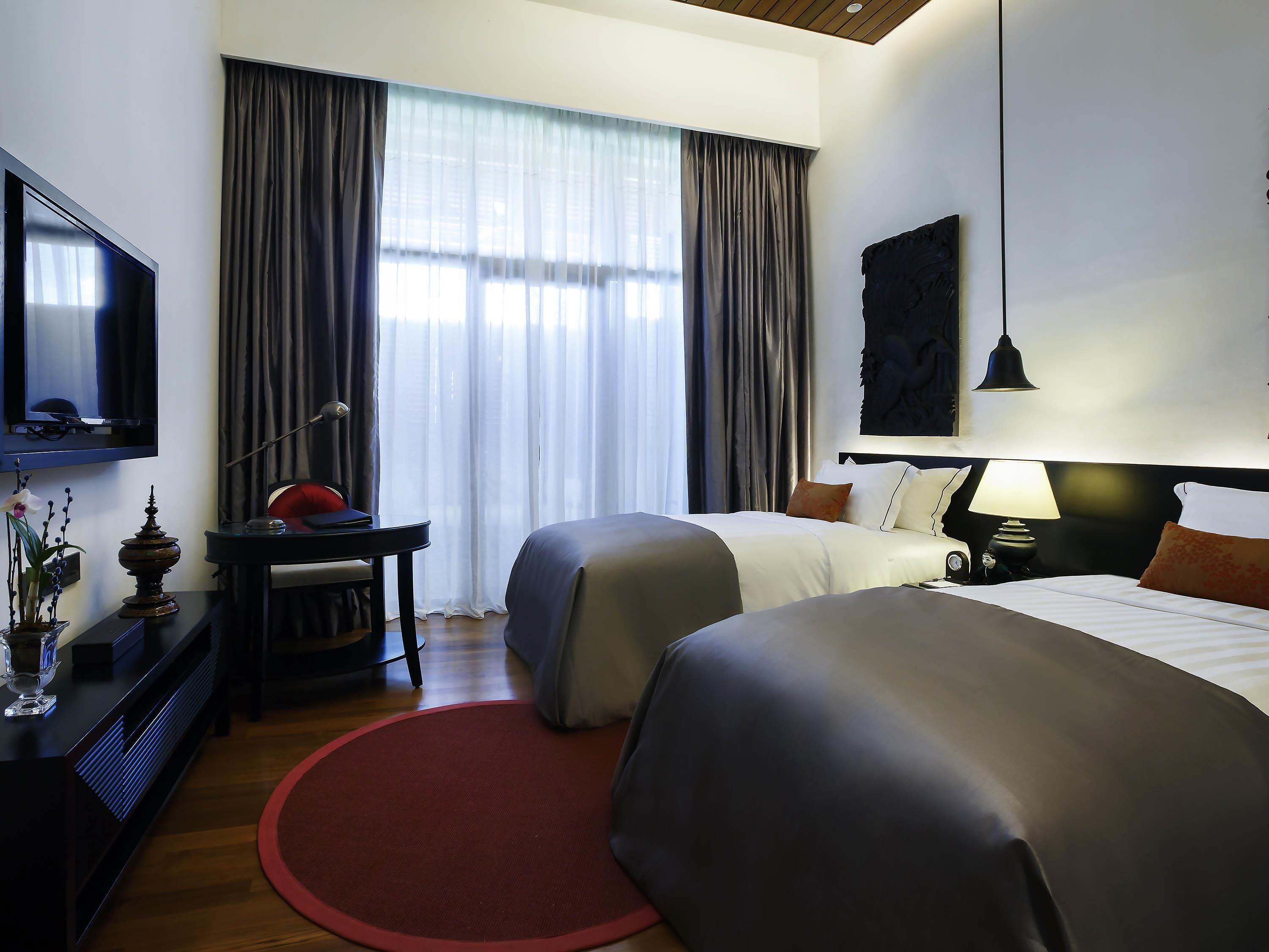 Habitación de hotel con dos camas, un escritorio con lámpara, televisión y un ventanal con cortinas.