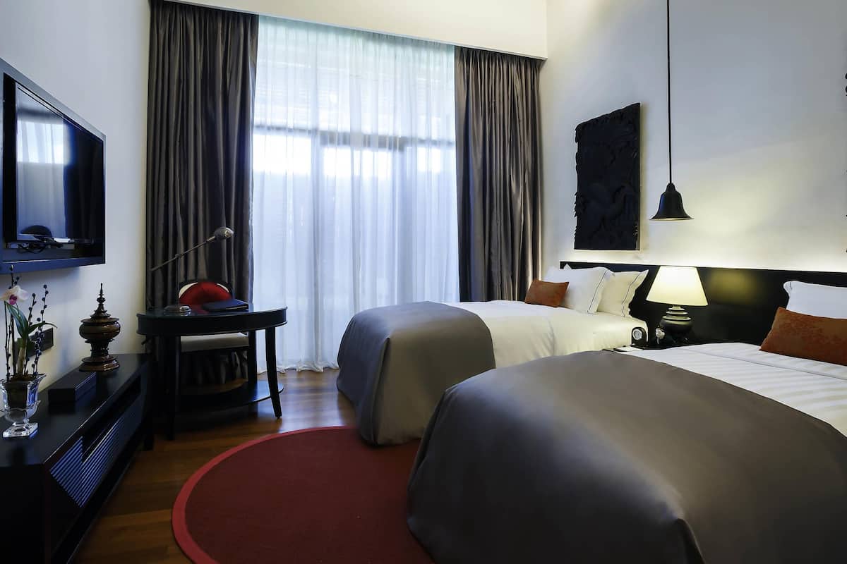 Habitación de hotel con dos camas, un escritorio con lámpara, televisión y un ventanal con cortinas.