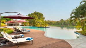 Un área junto a la piscina con sillones de descanso, sombrillas y una terraza de madera.