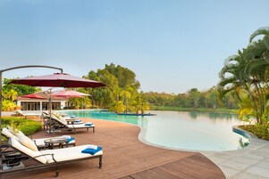 Un área junto a la piscina con sillones de descanso, sombrillas y una terraza de madera.