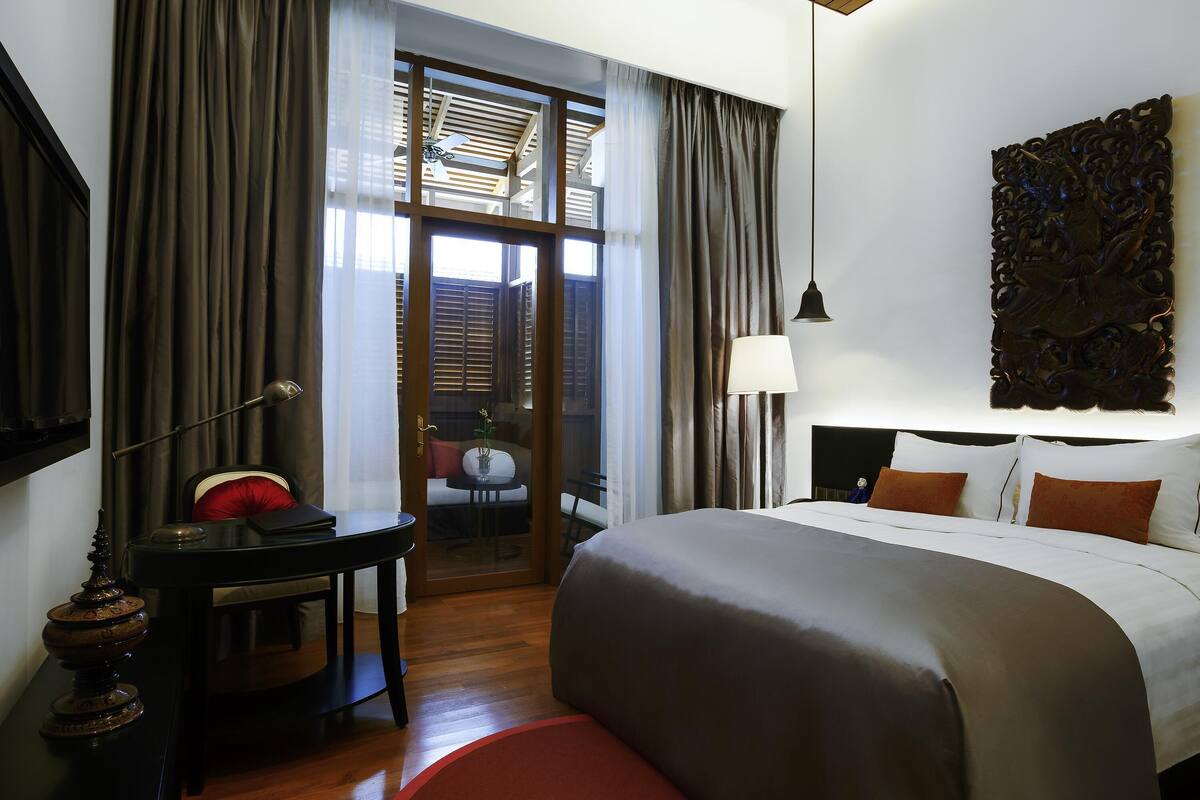 Habitación de hotel con una cama grande, un escritorio, una silla, una lámpara y vistas a través de un ventanal.