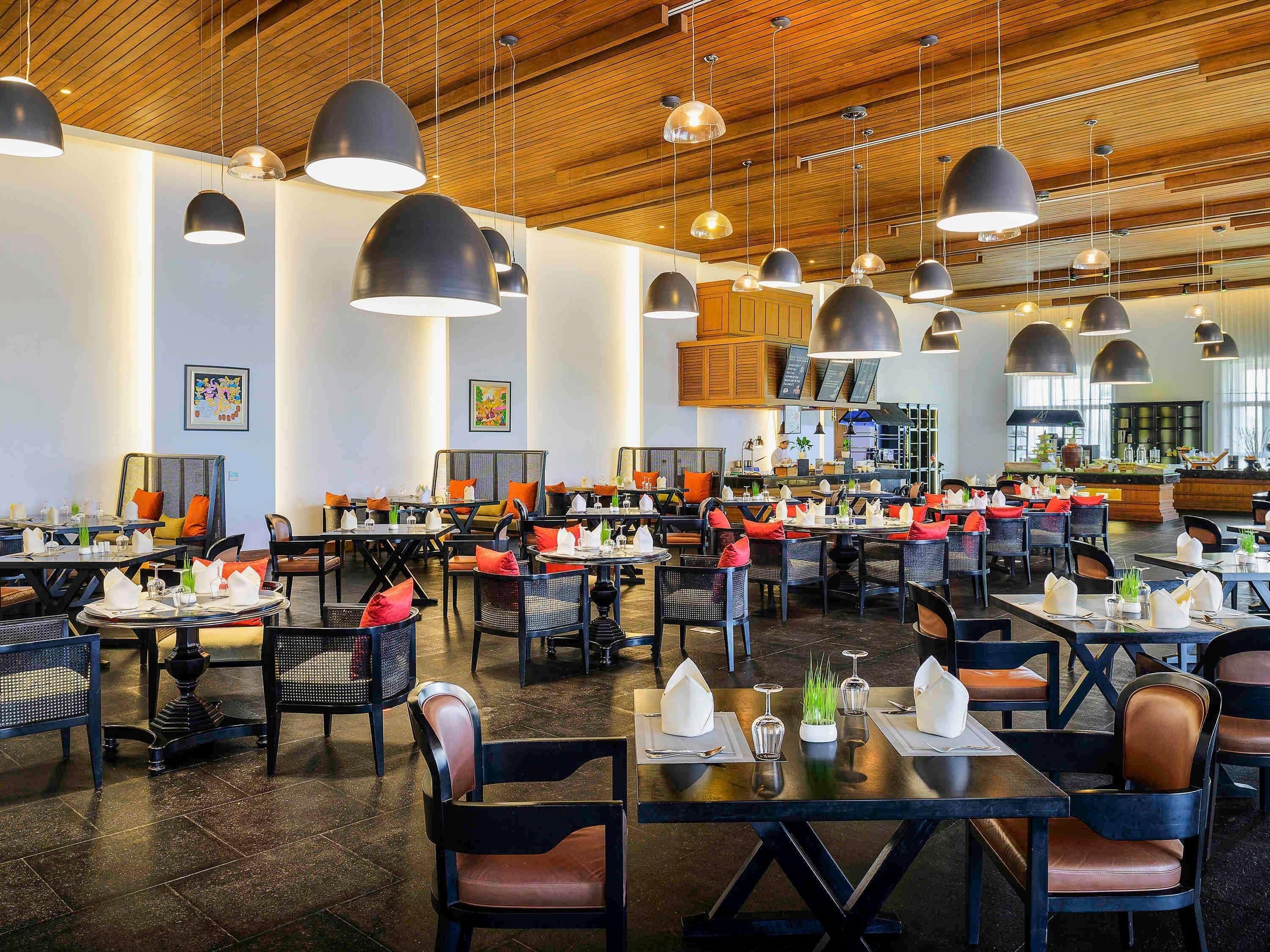 A spacious restaurant with multiple dining tables, black chairs, and pendant lighting.