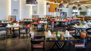 A spacious restaurant with multiple dining tables, black chairs, and pendant lighting.