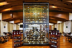 Un lobby de hotel espacioso con una estantería central para vinos, asientos cómodos y un techo moderno de madera.