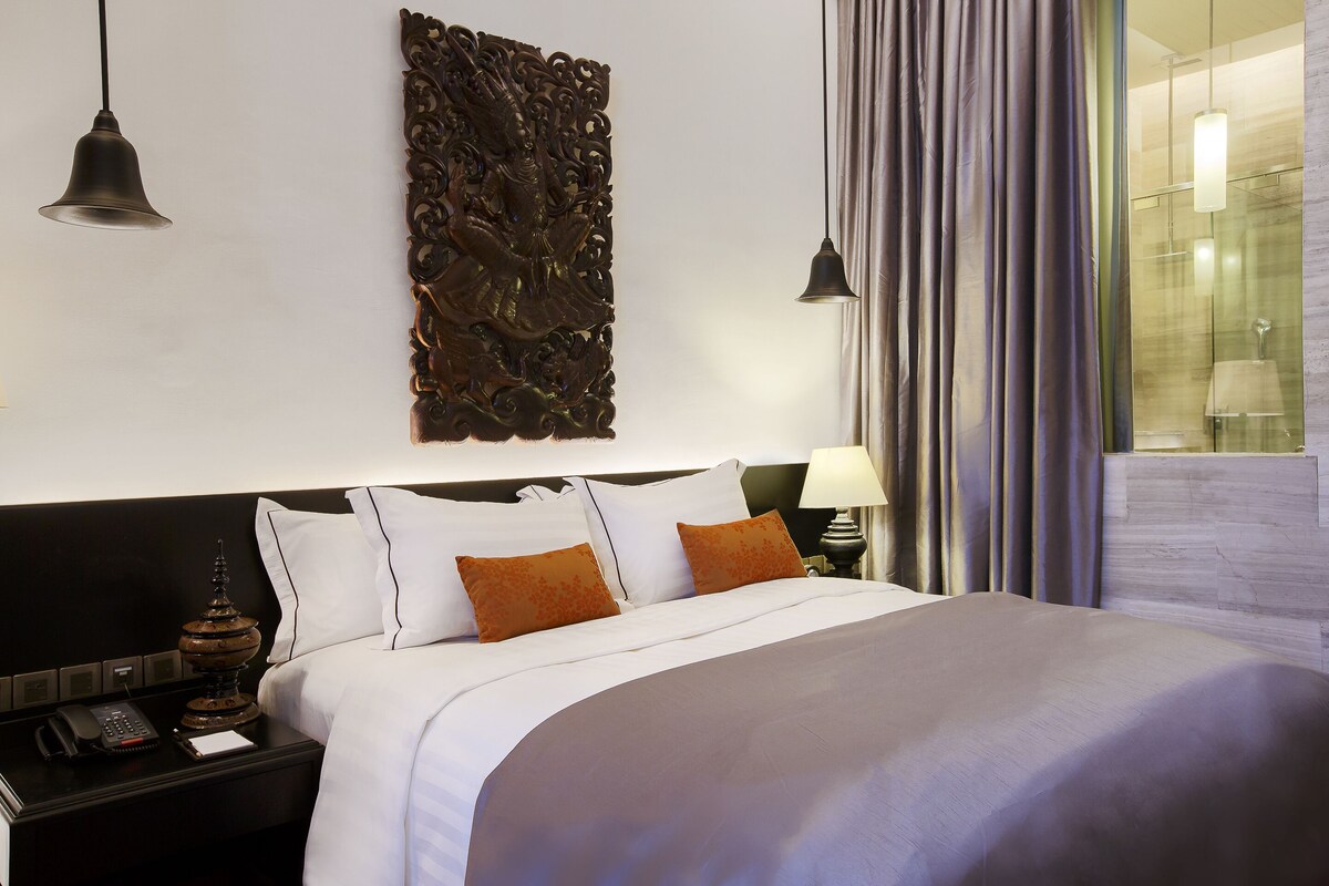 Une chambre d’hôtel avec un grand lit, une table de chevet avec un téléphone, un élément décoratif mural et une vue sur l’extérieur par une porte vitrée.