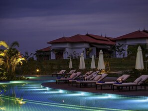 En swimmingpool med solstolar och parasoller, omgiven av en byggnad med ett rött tak.