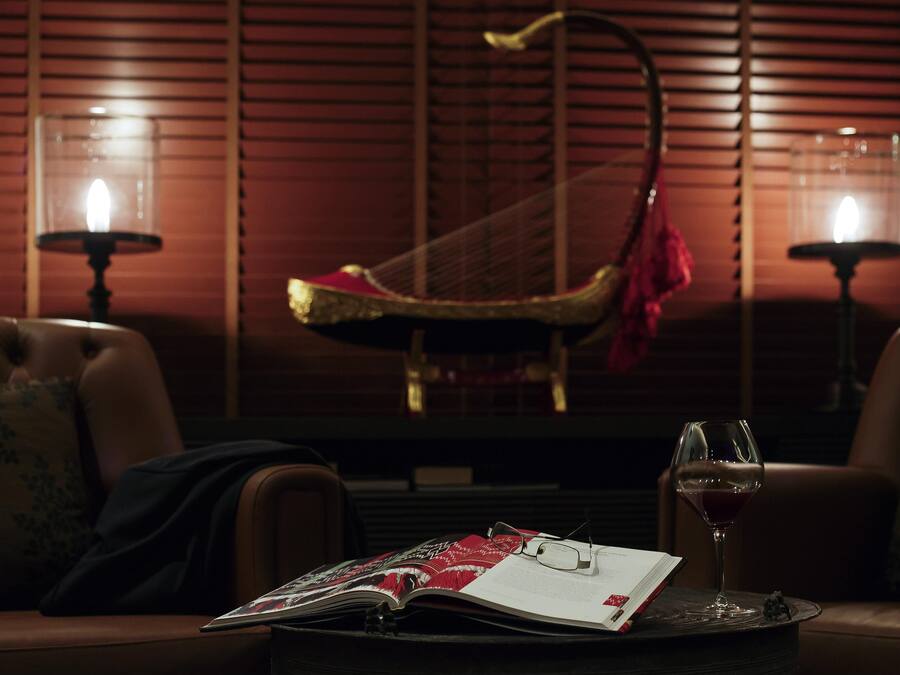 A dimly lit room with a harp, a glass of red wine, and an open magazine on a table.