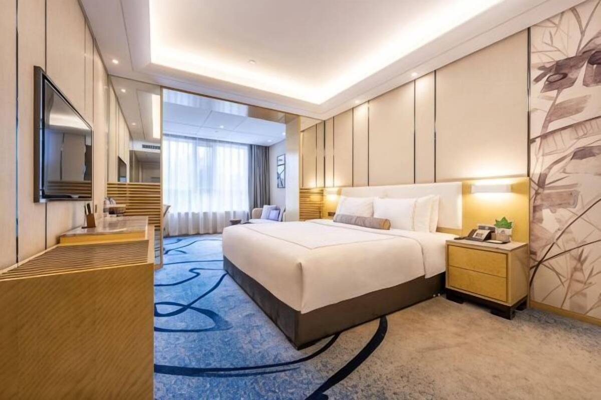 Una habitación de hotel con una cama grande, mesitas de noche, un televisor y un espejo.